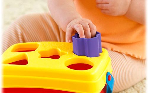 A baby playing with a toy where you match a shape to the hole it fits in.