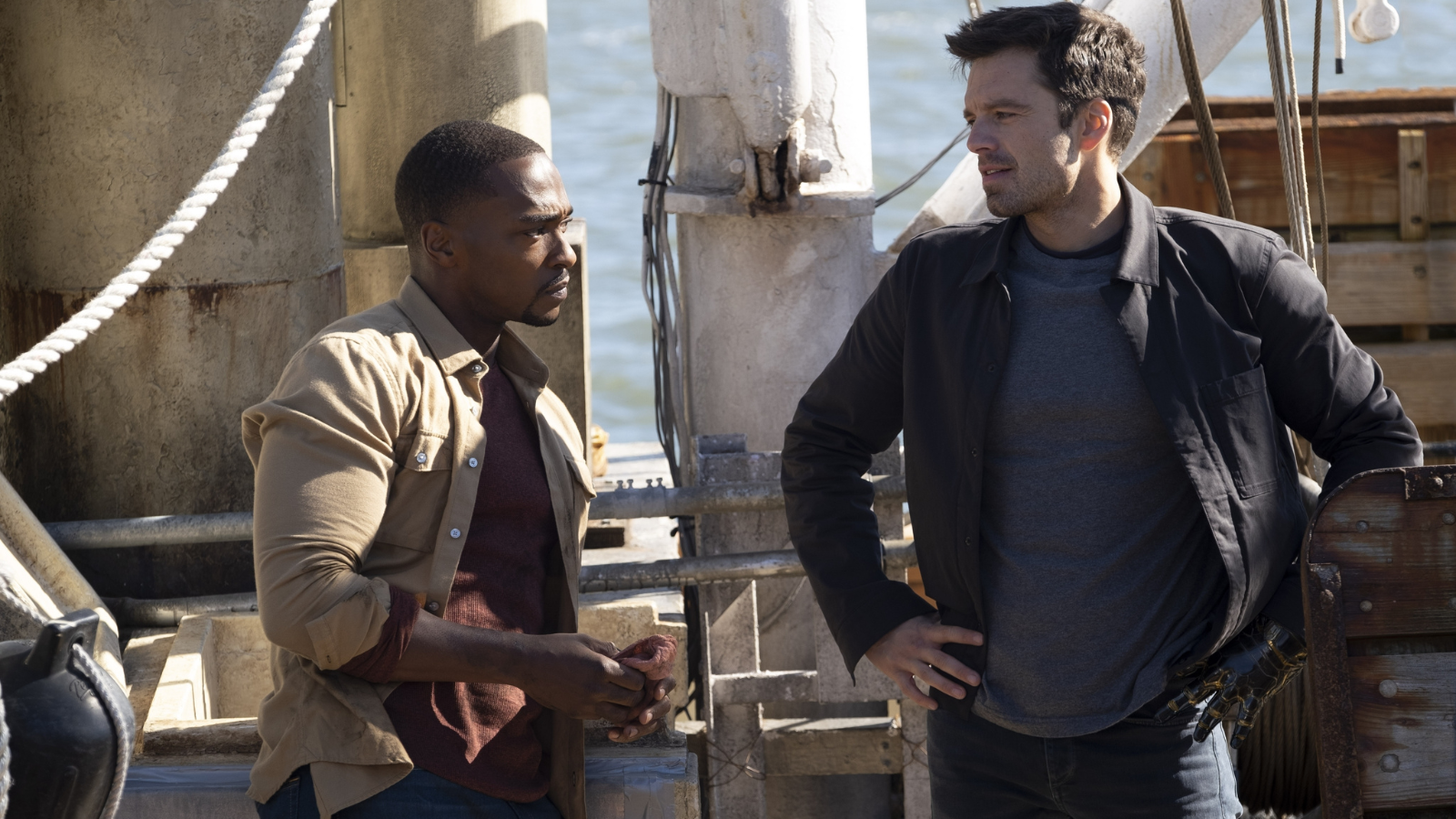 Sam and Bucky wearing shirts and light jackets while standing on a dock.