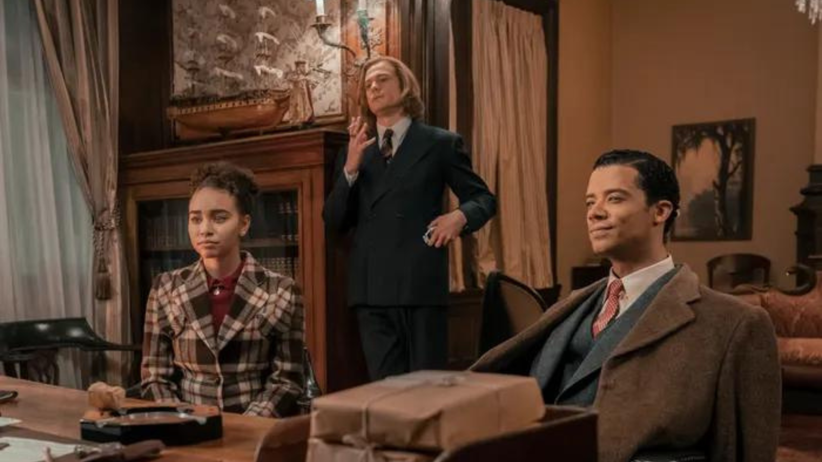 Claudia, Lestat, and Louis in a meeting. Claudia is in a plaid jacket, Lestat in a blue suit, Louis in a suit of differing blues and browns.