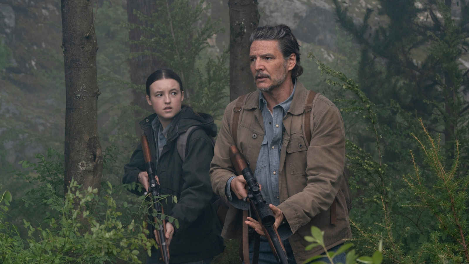 Bella Ramsey and Pedro Pascal holding guns in the woods. They are wearing shirts of similar shades of blue.