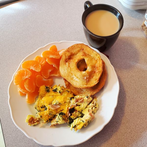 An image of a plate of food with orange sections, a bagel, and a frittata with a cup of tea beside the plate.